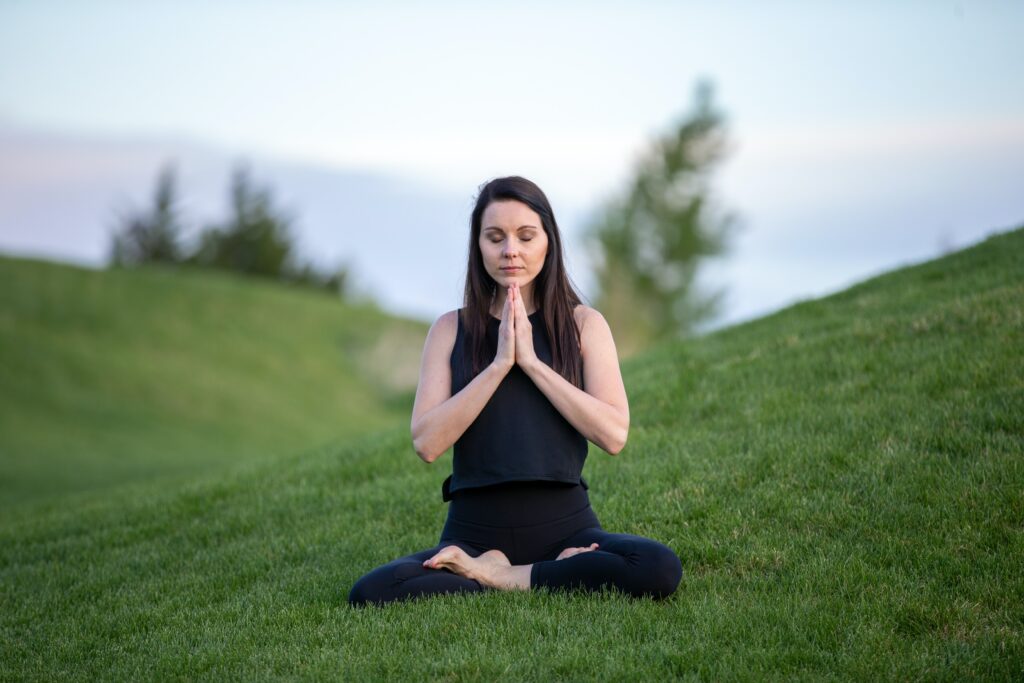 Woman in black yoga outfit meditating on the side of a grassy hill in nature