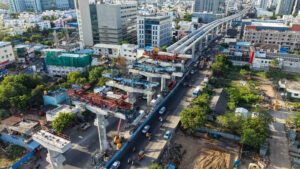 Aerial view of metro rail construction over busy city road with elevated track and urban buildings showing infrastructure development and public transport expansion