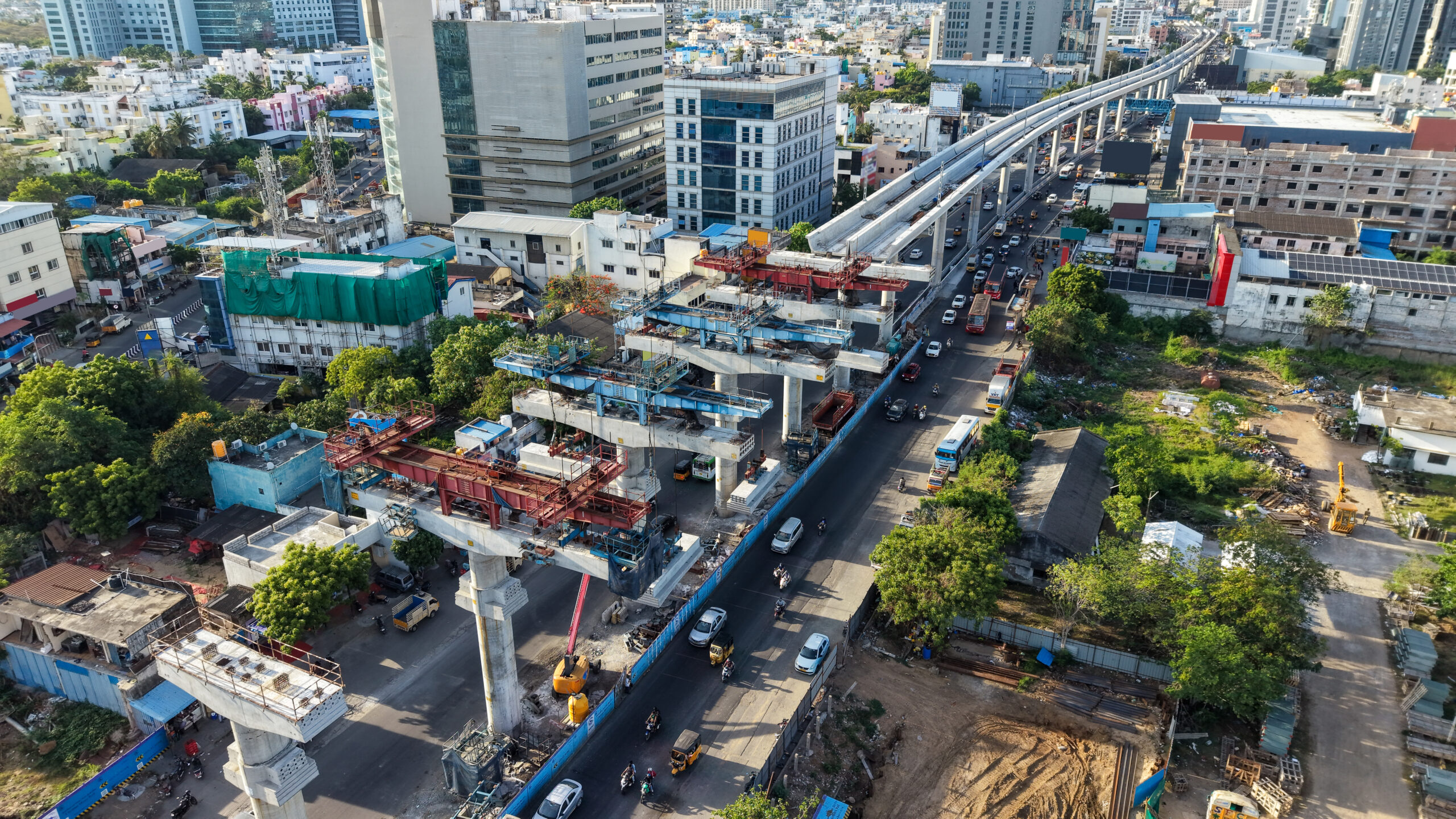 Aerial view of metro rail construction over busy city road with elevated track and urban buildings showing infrastructure development and public transport expansion