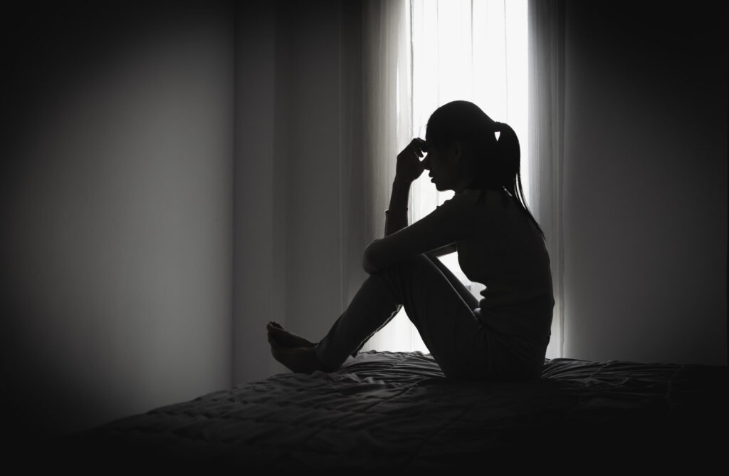 Depressed woman sitting alone in a dark room, representing domestic violence, emotional abuse, trauma, anxiety, loneliness, fear, and mental health struggles.
