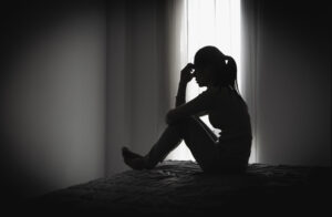 Depressed woman sitting alone in a dark room, representing domestic violence, emotional abuse, trauma, anxiety, loneliness, fear, and mental health struggles.