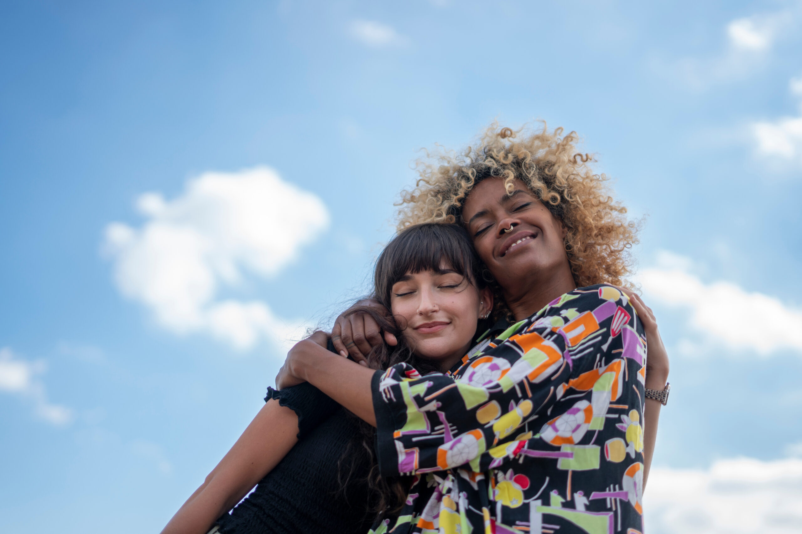 Female couple hugging against blue sky